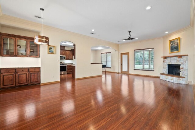 330 Arbors Cir, Elgin, TX 78621 - unfurnished living room featuring ceiling fan, dark wood-style floors, arched walkways, a fireplace, and crown molding