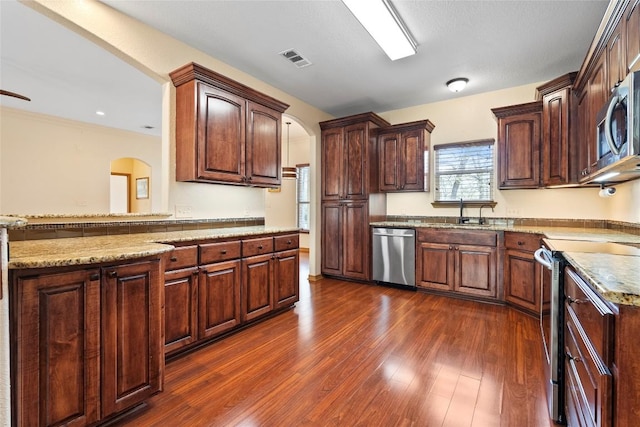 330 Arbors Cir, Elgin, TX 78621 - kitchen featuring stainless steel appliances, arched walkways, a sink, dark wood finished floors, and light stone countertops