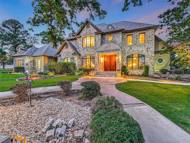 french provincial home with stone siding and a front yard
