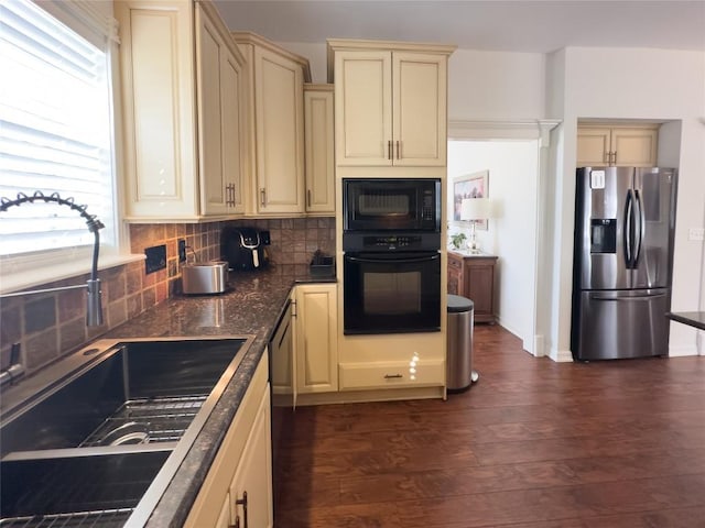 kitchen with a sink, dark wood-style floors, cream cabinets, dark countertops, and black appliances