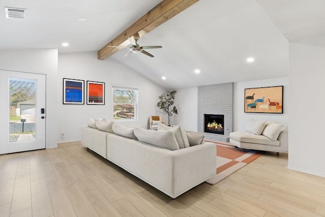 living room featuring a ceiling fan, lofted ceiling with beams, a fireplace, light wood-type flooring, and visible vents