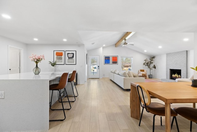 dining space with a brick fireplace, recessed lighting, light wood-style floors, a ceiling fan, and vaulted ceiling with beams