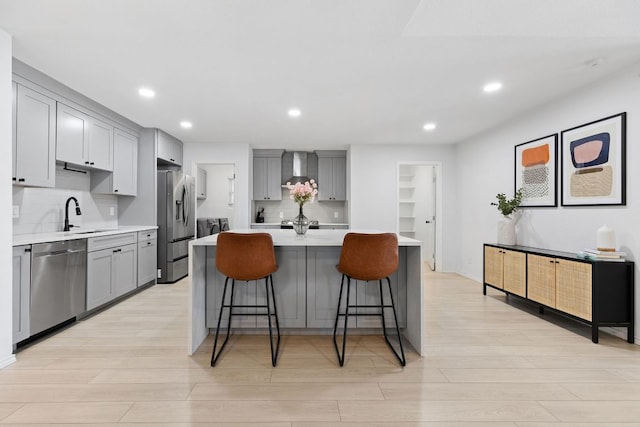 kitchen with light countertops, gray cabinets, stainless steel appliances, a sink, and wall chimney exhaust hood