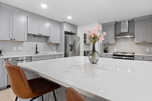 kitchen featuring a sink, gray cabinets, wall chimney exhaust hood, and appliances with stainless steel finishes