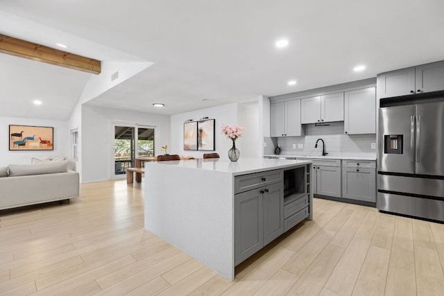 kitchen featuring decorative backsplash, light countertops, stainless steel refrigerator with ice dispenser, open floor plan, and gray cabinetry