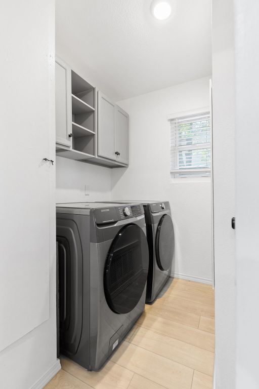 laundry room with baseboards, cabinet space, light wood-type flooring, and washer and clothes dryer