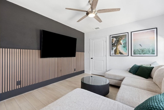 living area featuring wood finished floors, a wainscoted wall, ceiling fan, and visible vents