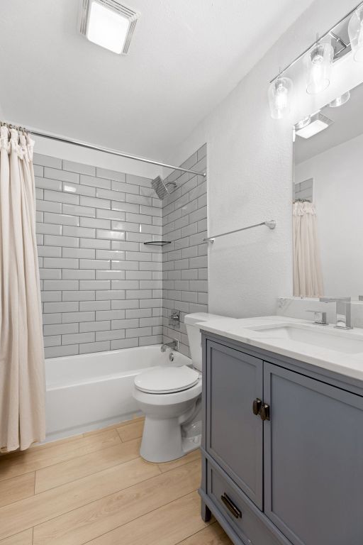 bathroom with vanity, shower / tub combo, toilet, visible vents, and wood finished floors