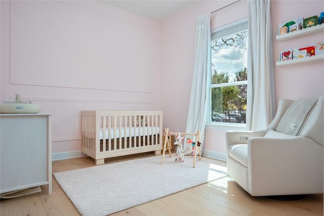 bedroom featuring baseboards, a nursery area, and wood finished floors