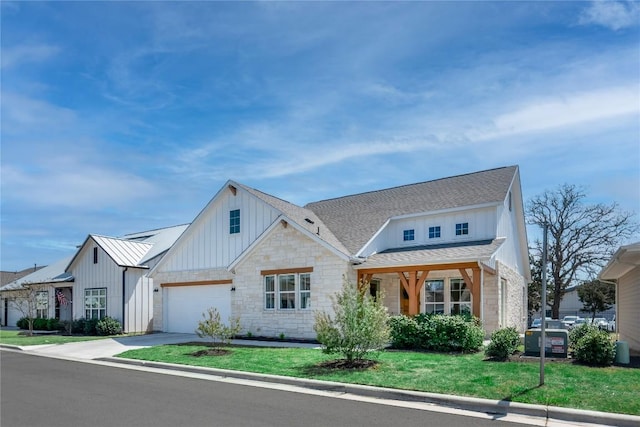 modern farmhouse featuring stone siding, concrete driveway, a front lawn, board and batten siding, and roof with shingles
