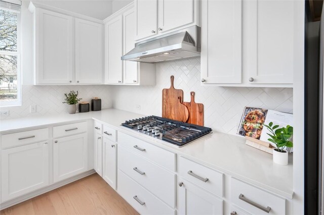 kitchen featuring light countertops, white cabinetry, tasteful backsplash, stainless steel gas stovetop, and under cabinet range hood