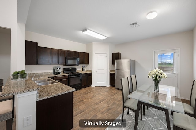 3603 Canaan Matthew Dr, Austin, TX 78725 - kitchen featuring black appliances, dark brown cabinetry, wood finished floors, a peninsula, and light stone counters