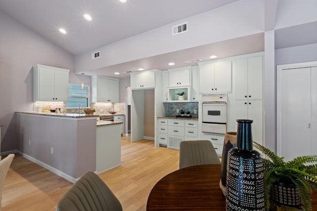 8702 Willowick Dr, Austin, TX 78759 - kitchen with white oven, a warming drawer, backsplash, vaulted ceiling, and a peninsula