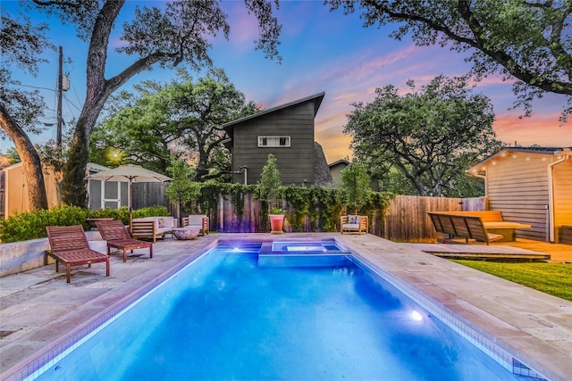 pool at dusk with a fenced backyard, an outdoor structure, a storage unit, and a pool with connected hot tub