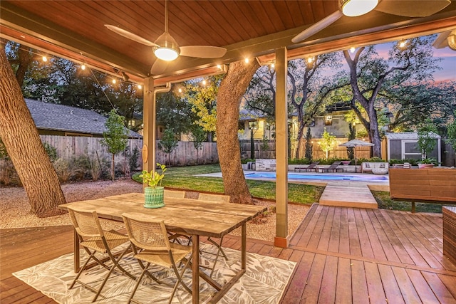 deck at dusk with a fenced backyard, a storage shed, outdoor dining space, and an outdoor structure