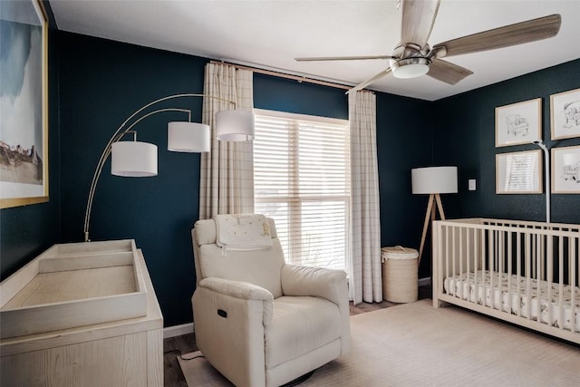 bedroom featuring baseboards, a ceiling fan, a crib, and wood finished floors