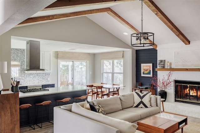 living room with a brick fireplace, beam ceiling, wood finished floors, high vaulted ceiling, and an inviting chandelier
