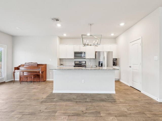 709 Bluffview Dr, Bastrop, TX 78602 - kitchen with stainless steel appliances, a chandelier, decorative backsplash, a center island with sink, and white cabinets