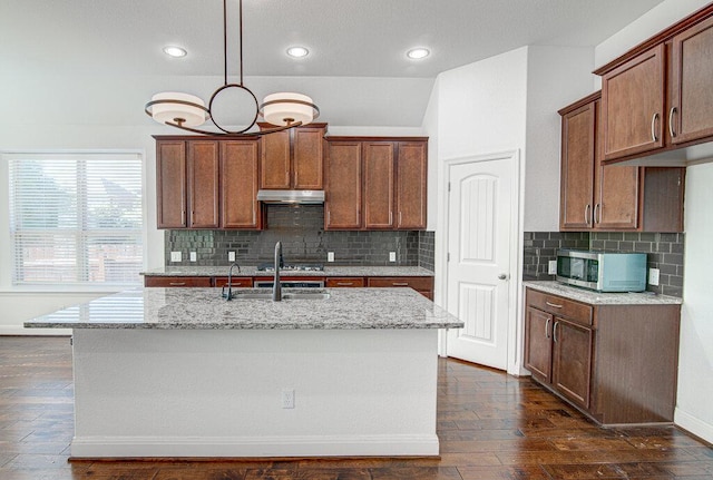 5617 Rio Chama Cv, Austin, TX 78738 - kitchen featuring under cabinet range hood, stainless steel microwave, light stone counters, dark wood-type flooring, and backsplash