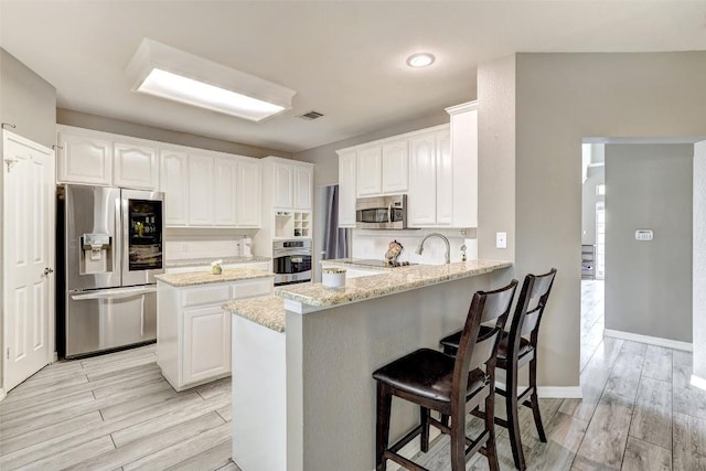 30003 Oakland Hills Dr, Georgetown, TX 78628 - kitchen with appliances with stainless steel finishes, a peninsula, light wood-style flooring, and white cabinetry