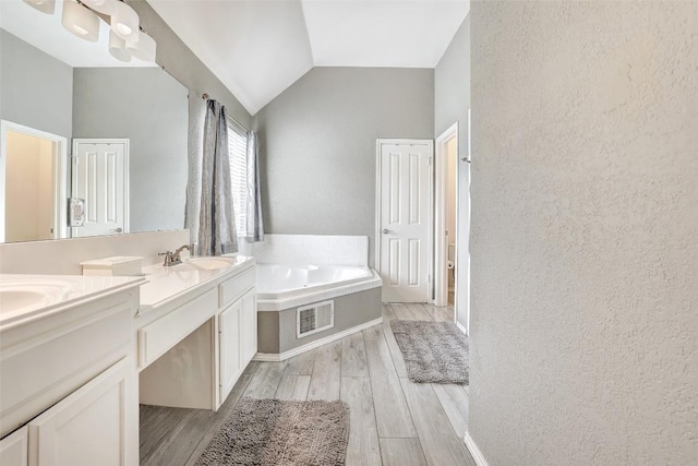 30003 Oakland Hills Dr, Georgetown, TX 78628 - bathroom featuring a bath, double vanity, wood finished floors, vaulted ceiling, and a textured wall