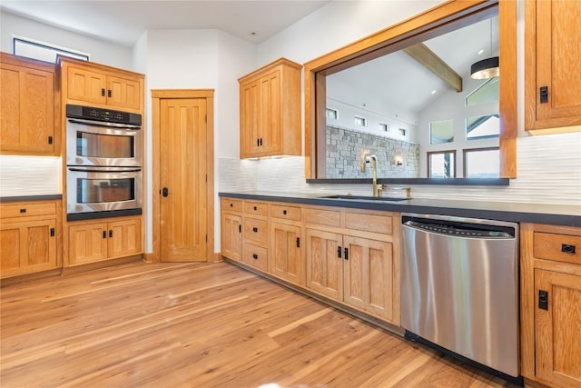 kitchen with a sink, dark countertops, light wood-style floors, and stainless steel appliances