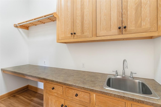 kitchen featuring built in study area, light brown cabinets, a sink, and wood finished floors
