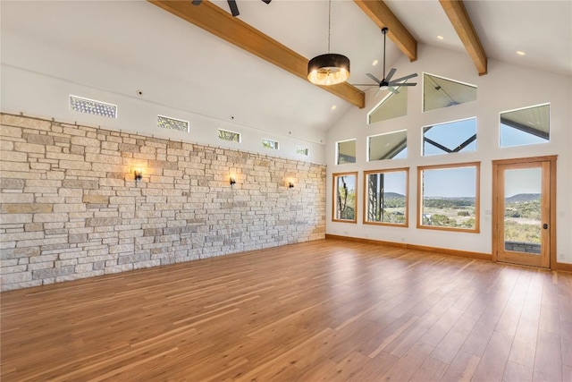 unfurnished living room with beamed ceiling, ceiling fan, high vaulted ceiling, and wood finished floors