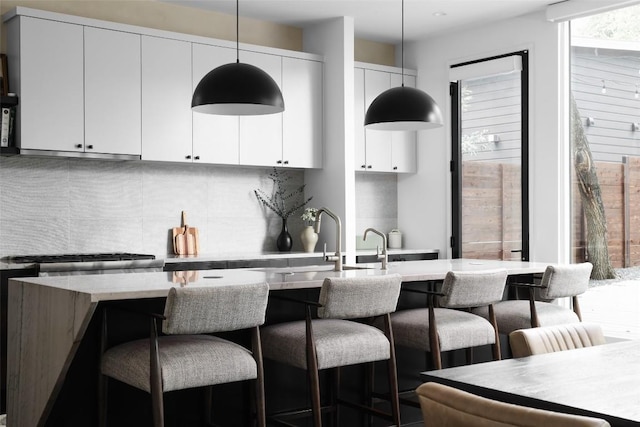 1105 W Monroe St, Austin, TX 78704 - kitchen featuring a breakfast bar area, hanging light fixtures, decorative backsplash, white cabinets, and a sink