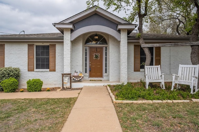 property entrance featuring a shingled roof and brick siding