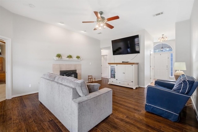 living room featuring ceiling fan with notable chandelier, a fireplace, dark wood finished floors, baseboards, and visible vents