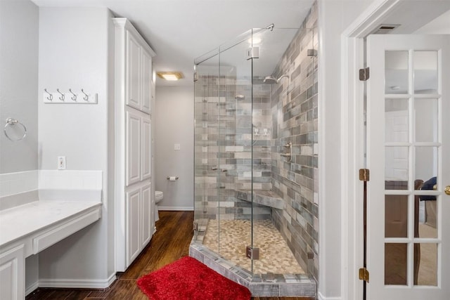 bathroom with toilet, wood finished floors, visible vents, and a stall shower