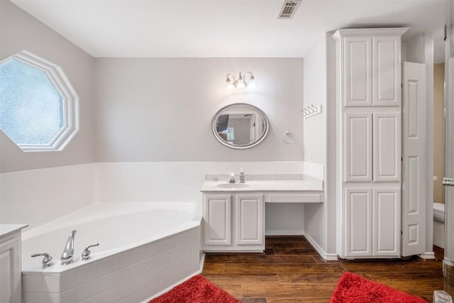 full bathroom featuring wood finished floors, a bath, vanity, toilet, and visible vents