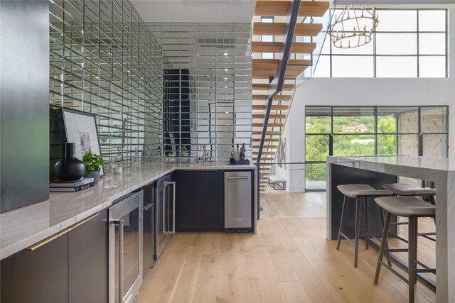 2701 Toro Canyon Rd Unit B, Austin, TX 78746 - indoor wet bar featuring beverage cooler, light wood-type flooring, a chandelier, and a towering ceiling