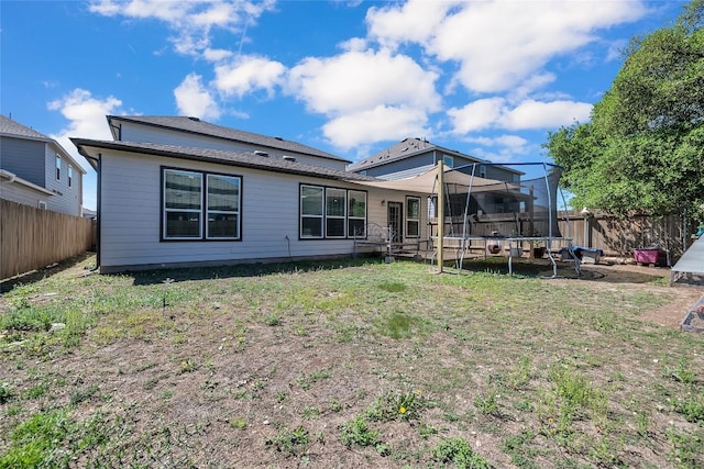rear view of house with a fenced backyard, a trampoline, and a lawn