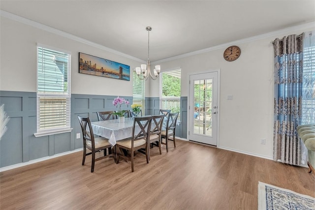 dining room featuring ornamental molding, a decorative wall, a notable chandelier, and wood finished floors