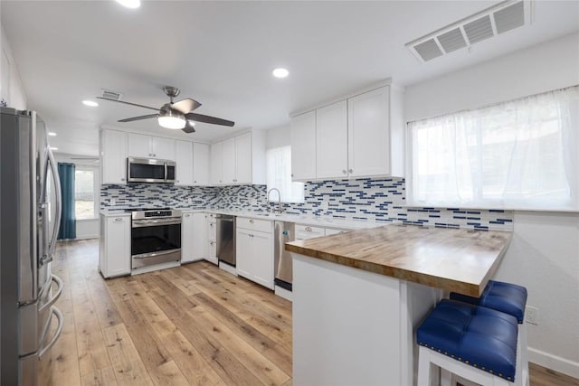 12300 Cassady Dr, Austin, TX 78727 - kitchen with appliances with stainless steel finishes, a peninsula, a ceiling fan, decorative backsplash, and white cabinetry