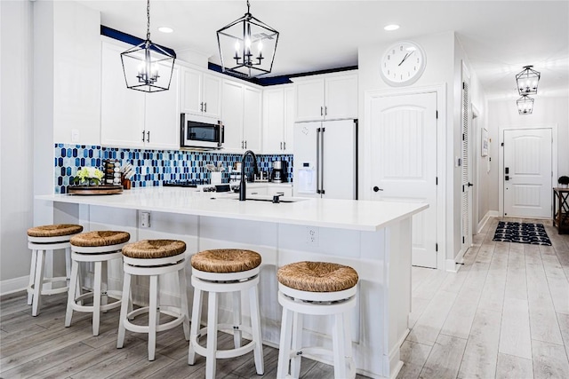 96 Island Dr Unit 44, Horseshoe Bay, TX 78657 - kitchen with white fridge with ice dispenser, stainless steel microwave, a peninsula, light wood finished floors, and a kitchen bar