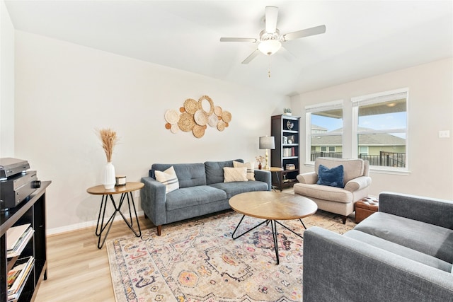 living area with light wood-style floors, a ceiling fan, and baseboards