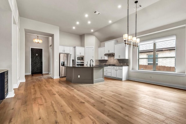 kitchen with a chandelier, stainless steel appliances, dark countertops, under cabinet range hood, and white cabinetry