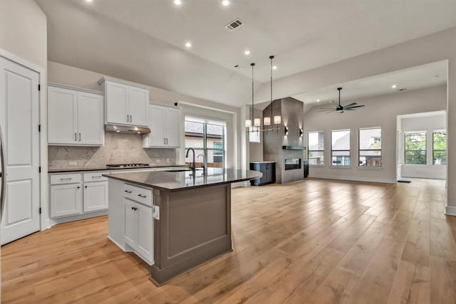 kitchen with dark countertops, backsplash, open floor plan, wall chimney exhaust hood, and healthy amount of natural light