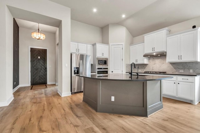 kitchen featuring stainless steel appliances, dark countertops, under cabinet range hood, backsplash, and lofted ceiling