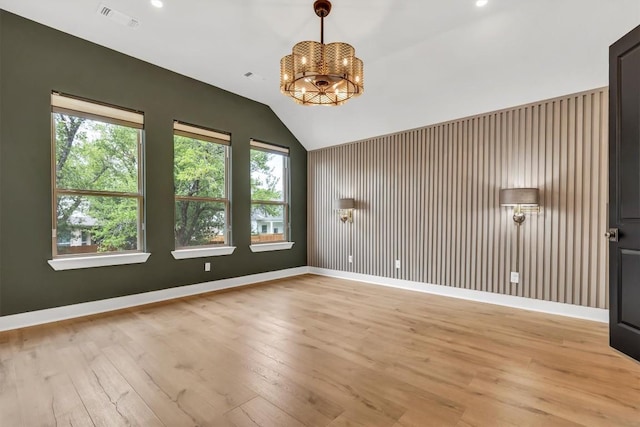 spare room featuring a chandelier, light wood-type flooring, vaulted ceiling, healthy amount of natural light, and baseboards