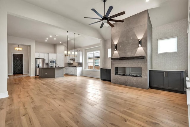 unfurnished living room featuring a chandelier, ceiling fan, vaulted ceiling, light wood finished floors, and a fireplace
