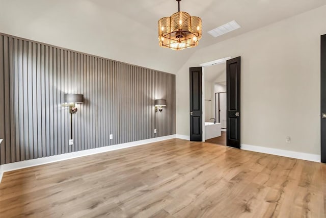 empty room with a chandelier, wood finished floors, lofted ceiling, and baseboards