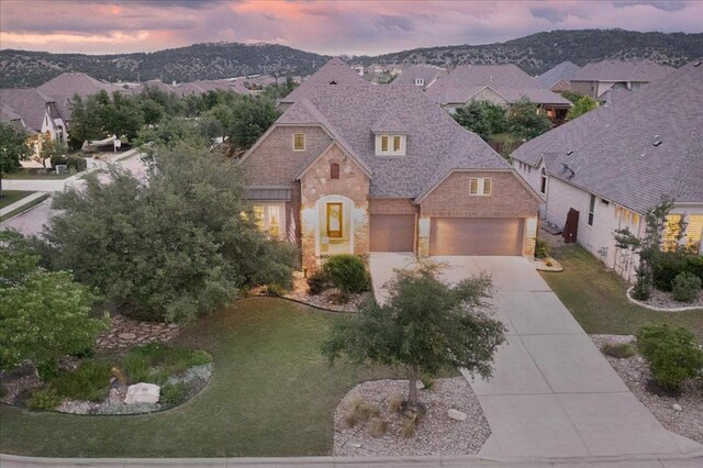 5701 Cherokee Draw Rd, Austin, TX 78738 - french country home with stone siding, concrete driveway, a front lawn, and brick siding