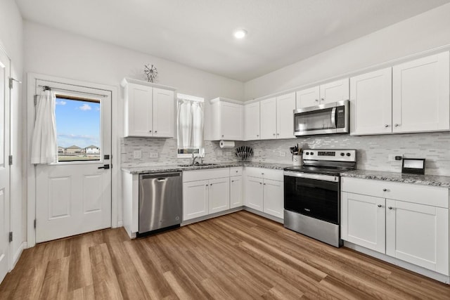 kitchen featuring white cabinetry, light stone countertops, appliances with stainless steel finishes, light wood-style floors, and decorative backsplash