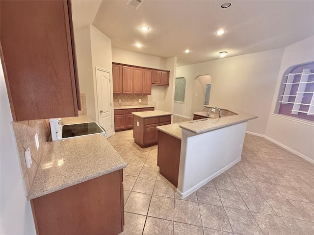 kitchen featuring arched walkways, range, light tile patterned floors, tasteful backsplash, and a center island with sink