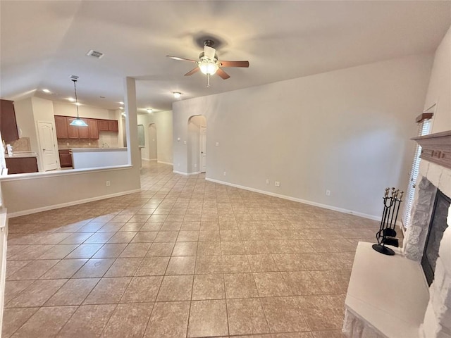 unfurnished living room with arched walkways, a glass covered fireplace, a ceiling fan, baseboards, and light tile patterned floors