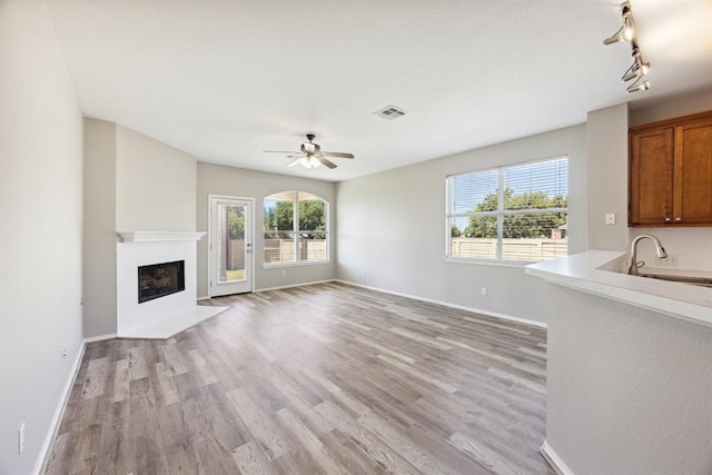 1606 Belvedere Pl, Round Rock, TX 78665 - unfurnished living room featuring light wood-type flooring, a sink, a fireplace with flush hearth, and a ceiling fan